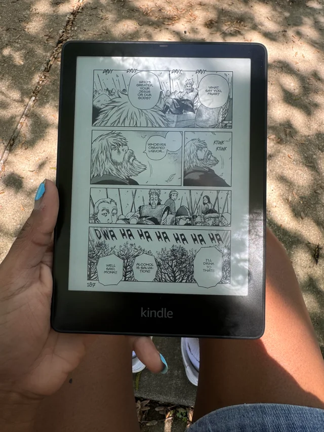 A reader held in one hand outdoors, showing a full manga page with speech bubbles and sound effects.